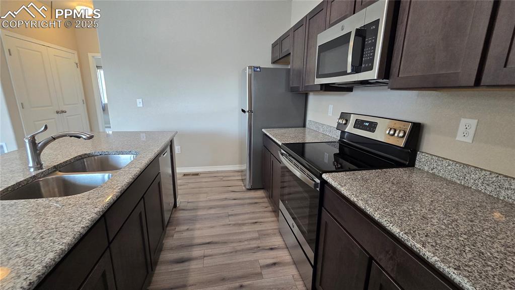 Image 19 of 29: Kitchen with stainless steel appliances, dark brown cabinets, light wood-st