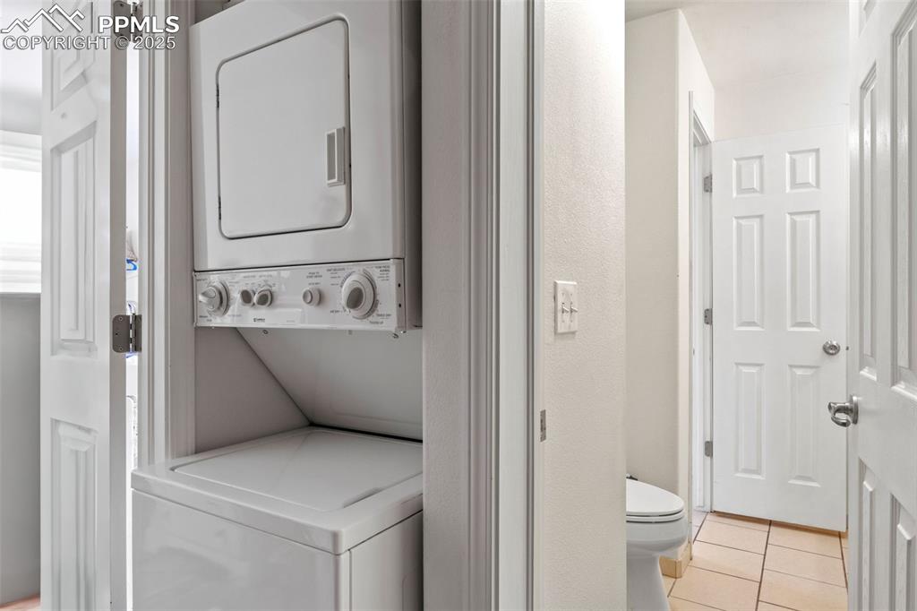 Image 18 of 21: Laundry room with stacked washer / drying machine and light tile patterned 