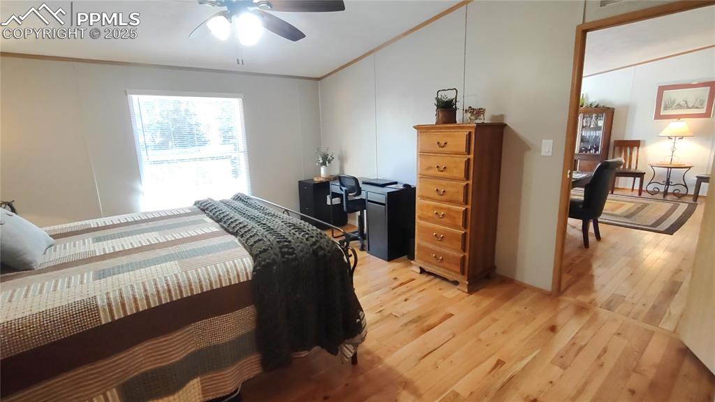 Image 18 of 42: Ceiling fan, oak flooring, and window with blinds in primary bedroom.