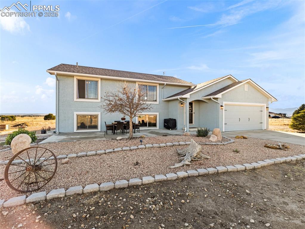 Caption: View of front of house featuring stucco siding, driveway, an attached garage, and a patio