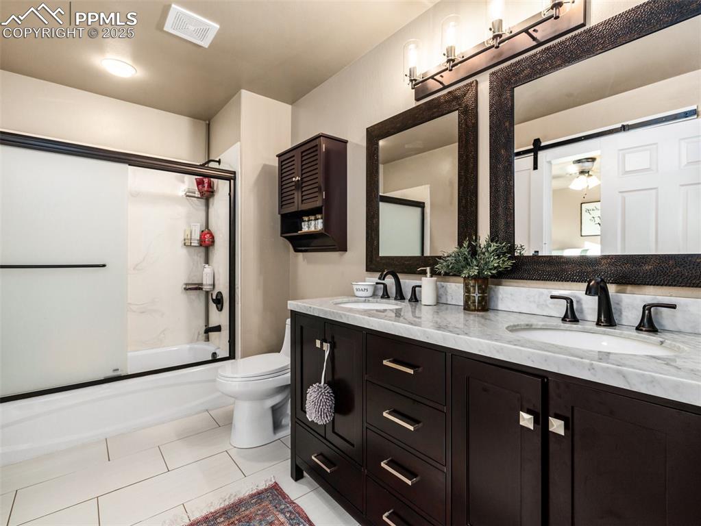 Image 23 of 41: Full bath with double vanity, combined bath / shower with glass door, and l