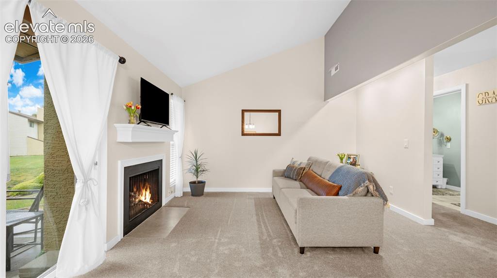 Image 12 of 37: Living area featuring a fireplace with a white mantel, carpeting, and a vau