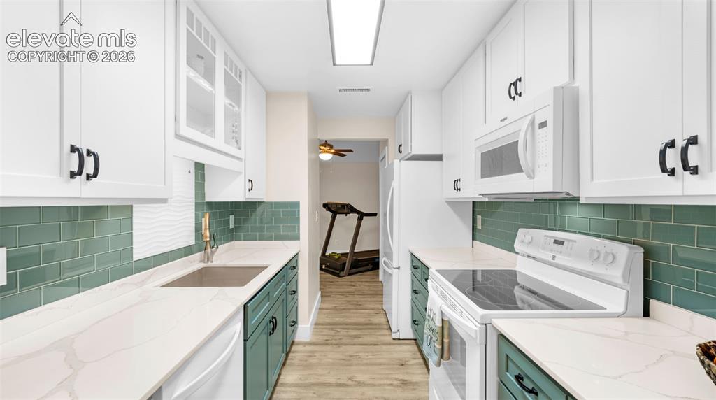 Image 17 of 37: Galley kitchen featuring white upper cabinetry, teal lower cabinetry, light
