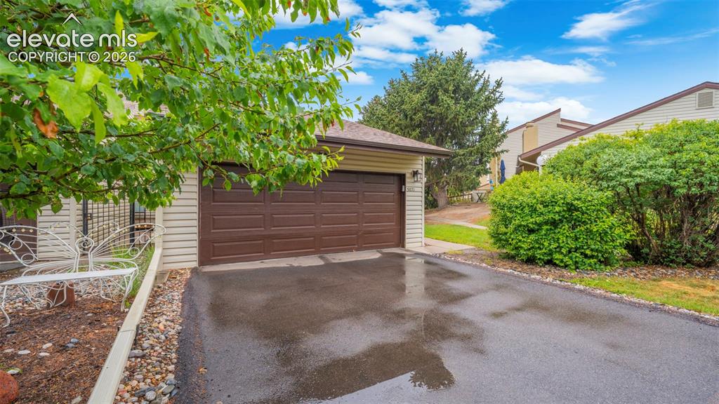 Image 2 of 37: Attached garage with a brown panel door, asphalt driveway, and side yard wi