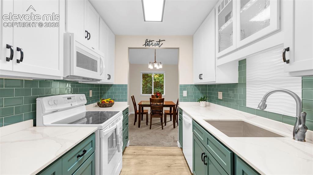 Image 21 of 37: Galley kitchen featuring white upper cabinetry, teal lower cabinetry, and w