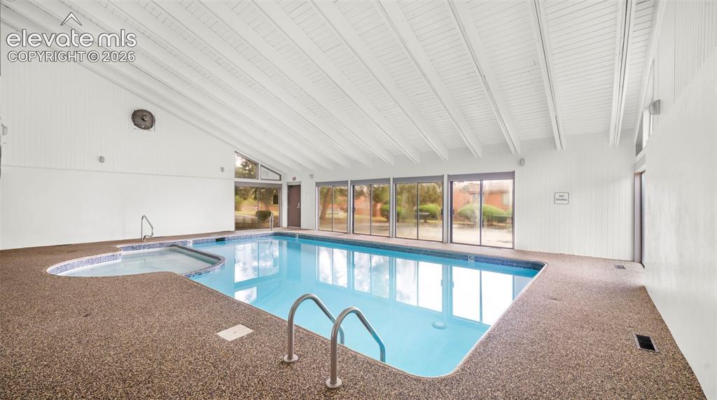 Image 32 of 37: Indoor swimming pool with an integrated spa, surrounded by stone-aggregate