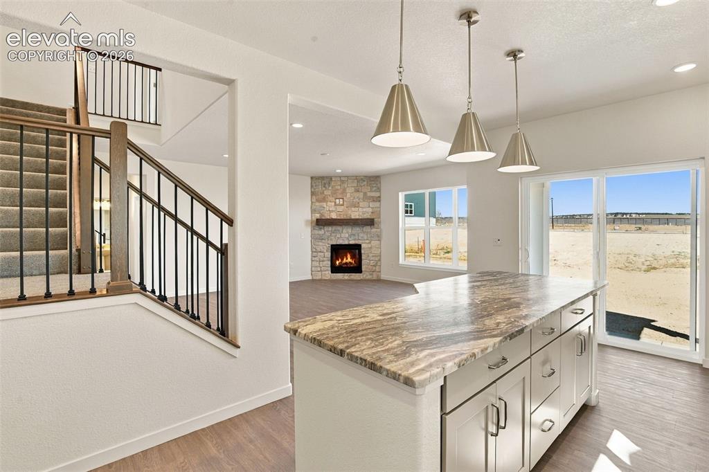 Image 14 of 50: Kitchen island with stone-finish countertop, three metal pendant lights, me