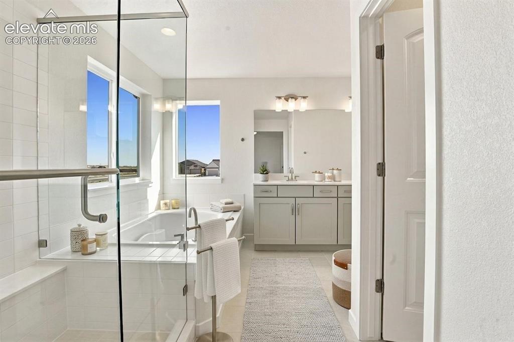 Image 27 of 50: Glass-enclosed shower with white wall tile, deep soaking tub, and vanity wi