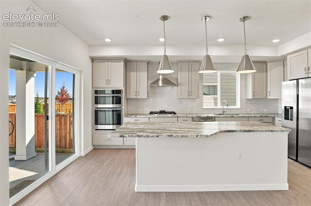 Image 8 of 50: Kitchen featuring a central island with stone-finish countertops, stainless