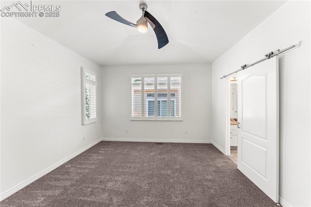 Image 17 of 50: Carpeted master bedroom with a ceiling fan and baseboards and barn door ent
