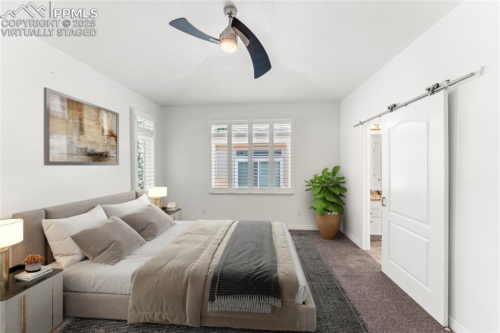 Image 18 of 50: Virtually staged carpeted bedroom featuring a barn door, a ceiling fan, and