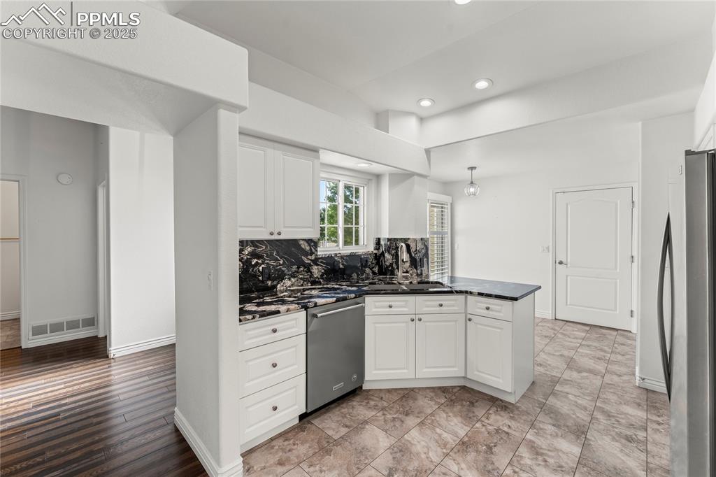 Image 25 of 50: Kitchen with stainless steel appliances, white cabinetry, a peninsula, back