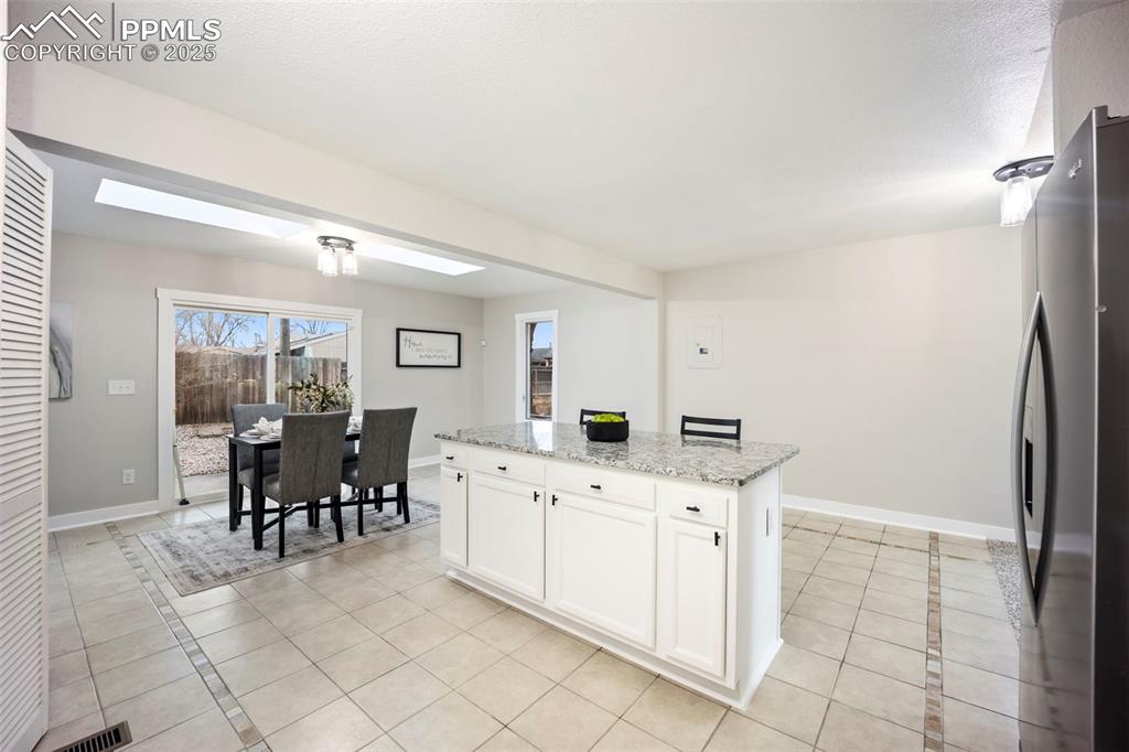 Image 12 of 33: Kitchen with white cabinetry, stainless steel fridge, light stone counterto