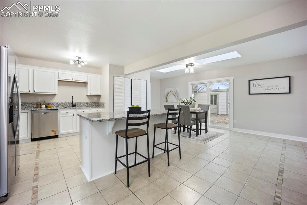 Image 9 of 33: Kitchen with light tile patterned floors, a skylight, white cabinets, a bre