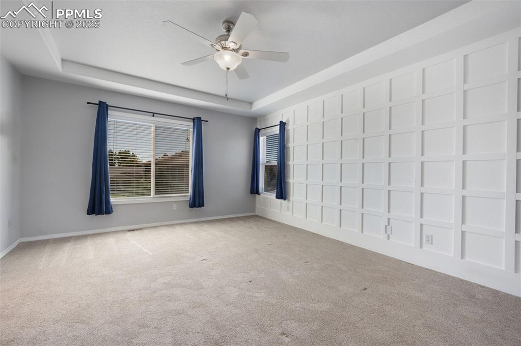 Image 25 of 46: Unfurnished room featuring a tray ceiling, light carpet, ceiling fan, and a