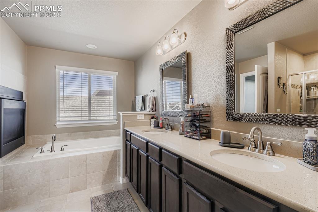 Image 16 of 35: Bathroom featuring double vanity, a bath, a textured wall, light tile patte