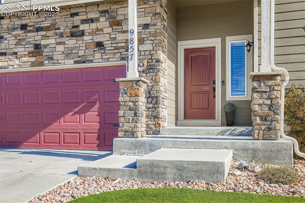 Image 3 of 35: Property entrance featuring stone siding, concrete driveway, and a porch