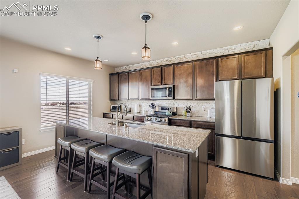 Image 8 of 35: Kitchen with dark brown cabinetry, stainless steel appliances, light stone 