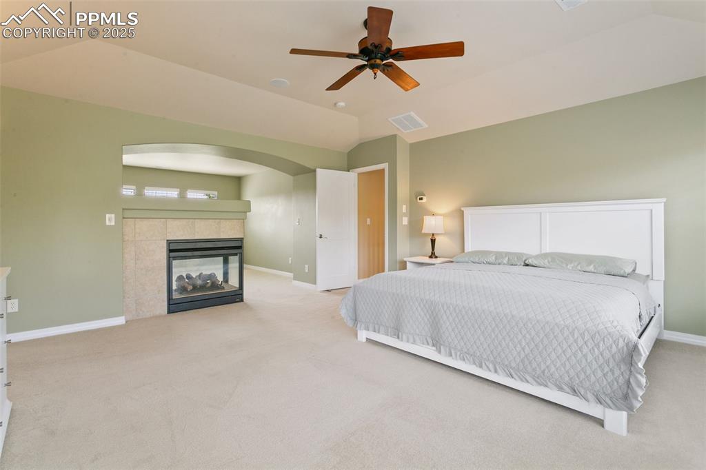 Image 19 of 37: Bedroom with lofted ceiling, light colored carpet, a fireplace, and a ceili