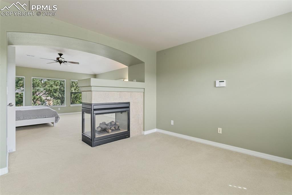 Image 20 of 37: Living area with light carpet, a tiled fireplace, and ceiling fan