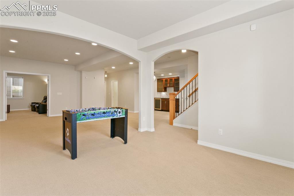 Image 30 of 37: Recreation room with arched walkways, recessed lighting, and light carpet