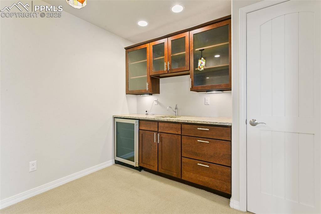 Image 33 of 37: Indoor wet bar with glass insert cabinets, light carpet, beverage cooler, l