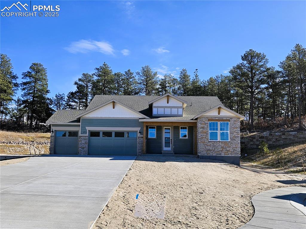 Caption: View of front of property featuring stone siding, a garage, concrete driveway, a shingled roof, and 