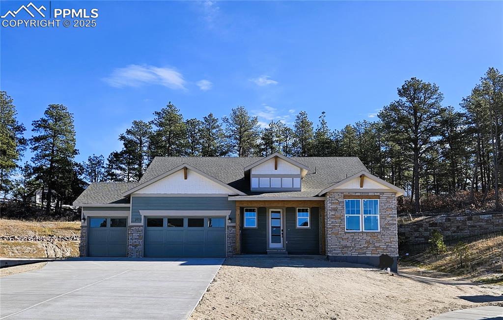 Image 2 of 10: View of front facade with stone siding, driveway, a garage, and a shingled 