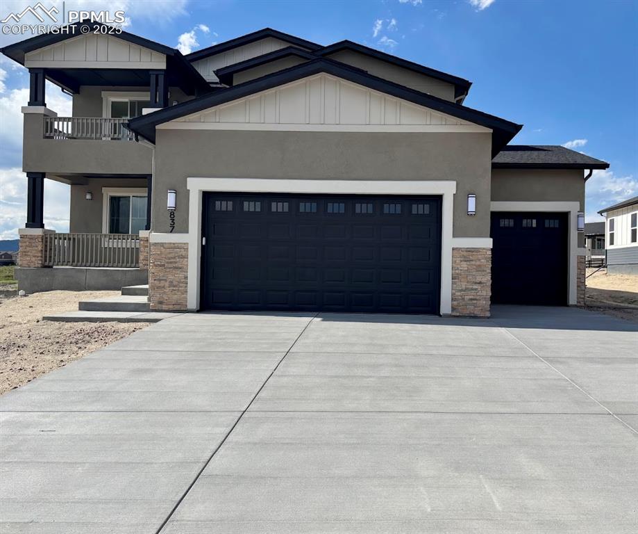 Caption: View of front facade featuring stone siding, a garage, driveway, stucco siding, and board and batten