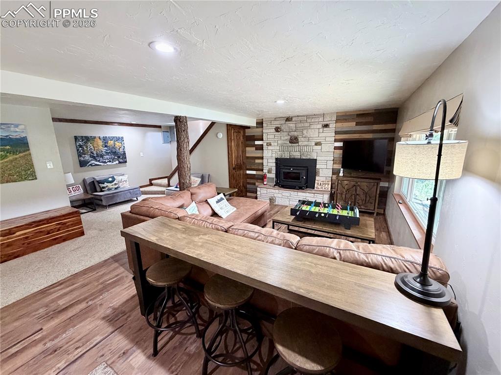Image 12 of 20: Living area with wood finished floors, a wood stove, stairway, and a textur