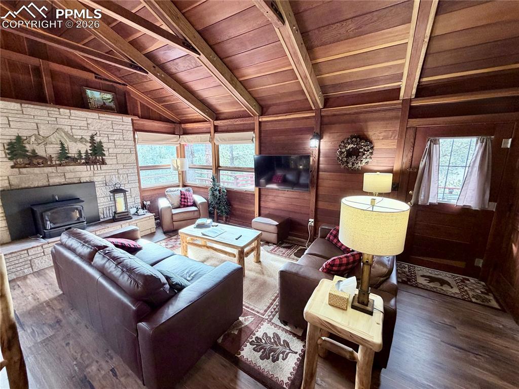 Image 6 of 20: Living area featuring a wood stove, wooden walls, wood finished floors, hea