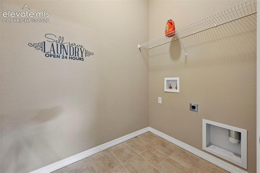 Image 16 of 37: Dedicated laundry space featuring tiled flooring, a wire shelf, and applian