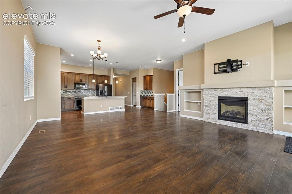 Image 8 of 37: Spacious living area featuring wood-finish flooring, a stone-accented firep