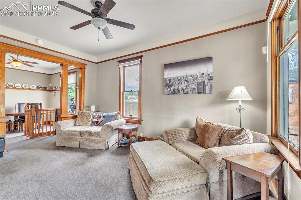 Image 6 of 49: Carpeted living area featuring a ceiling fan, crown molding, and ornate col