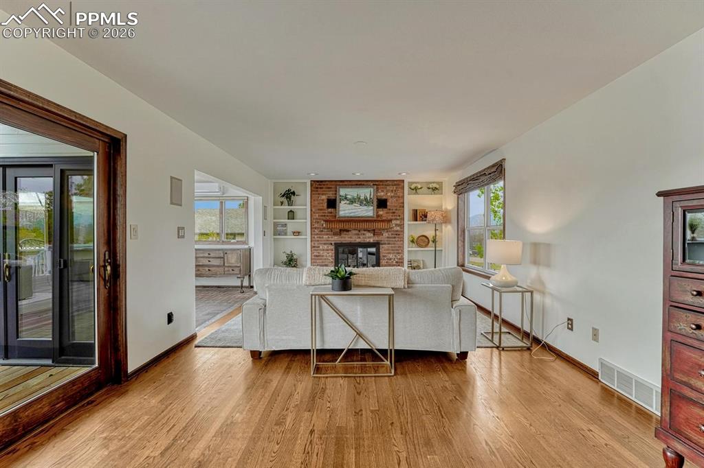 Image 15 of 44: Hardwood flooring extends throughout this expansive room, featuring a brick