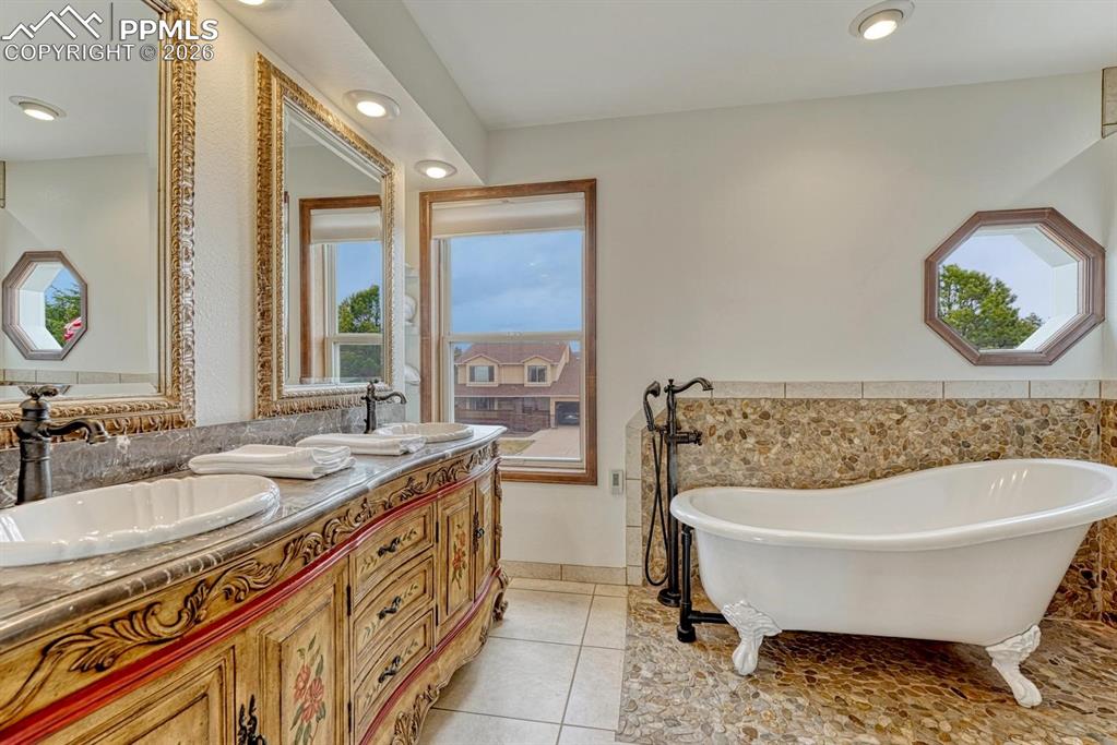 Image 29 of 44: Freestanding clawfoot tub and pebble tile flooring, alongside a double vani