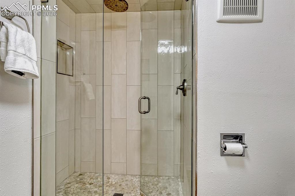 Image 38 of 44: Glass-enclosed shower featuring vertically oriented wall tiles and a pebble