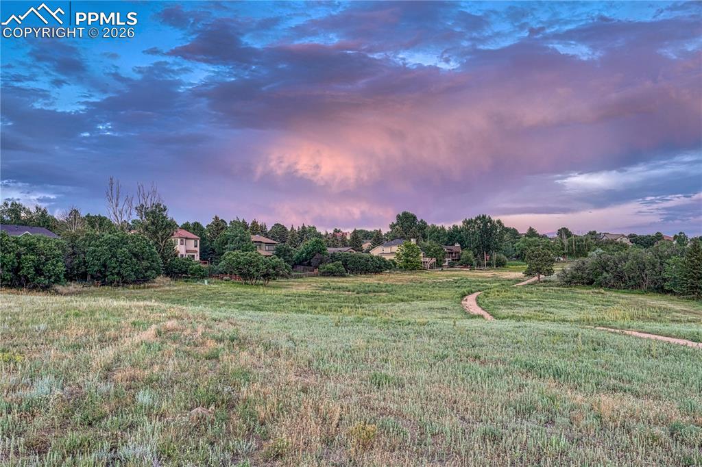 Image 42 of 44: Expansive open field with a winding dirt path, bordered by mature trees and