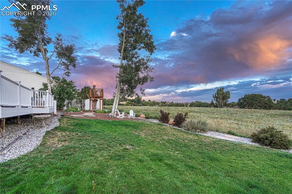 Image 44 of 44: Expansive backyard featuring a manicured lawn, a raised deck with white rai