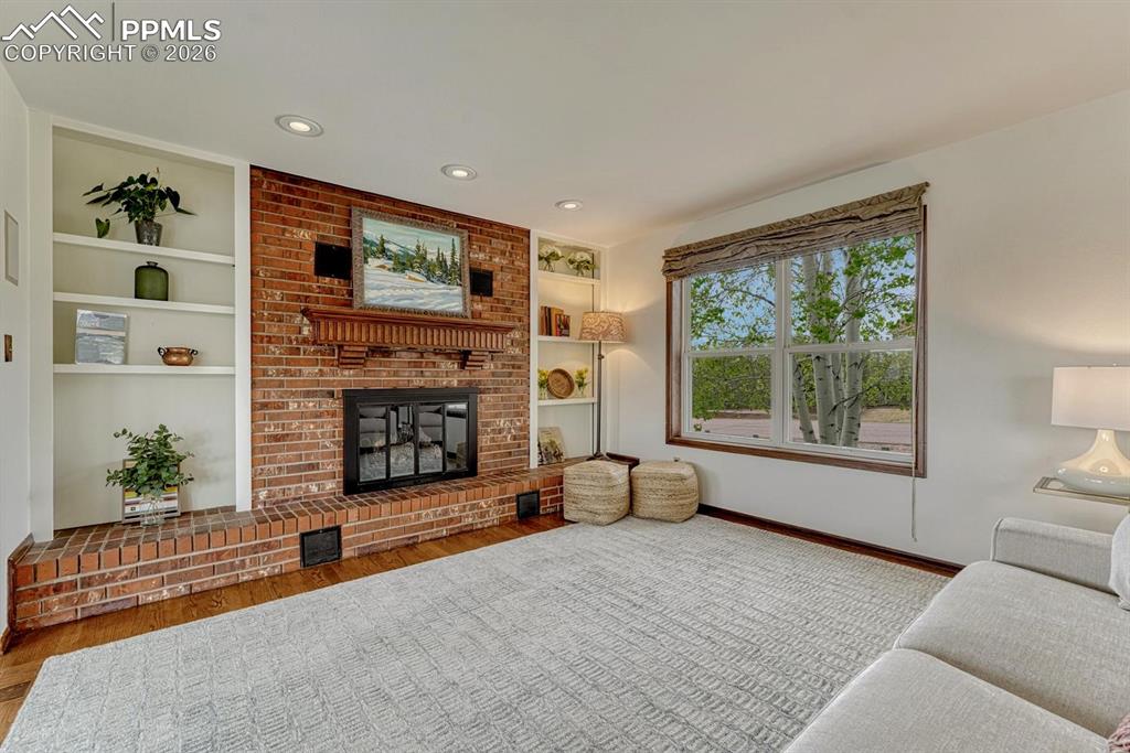 Image 7 of 44: Brick fireplace with a wood mantle and hearth, flanked by built-in shelving