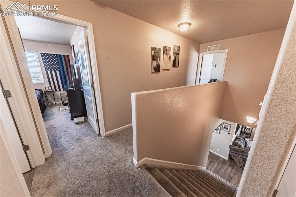 Image 17 of 33: Hallway featuring carpet, a textured ceiling, and an upstairs landing