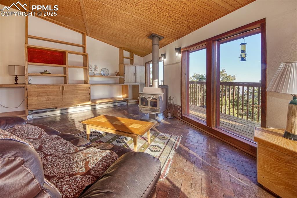 Image 5 of 33: Living room with lofted ceiling, a wood stove, brick floor, wood ceiling, a