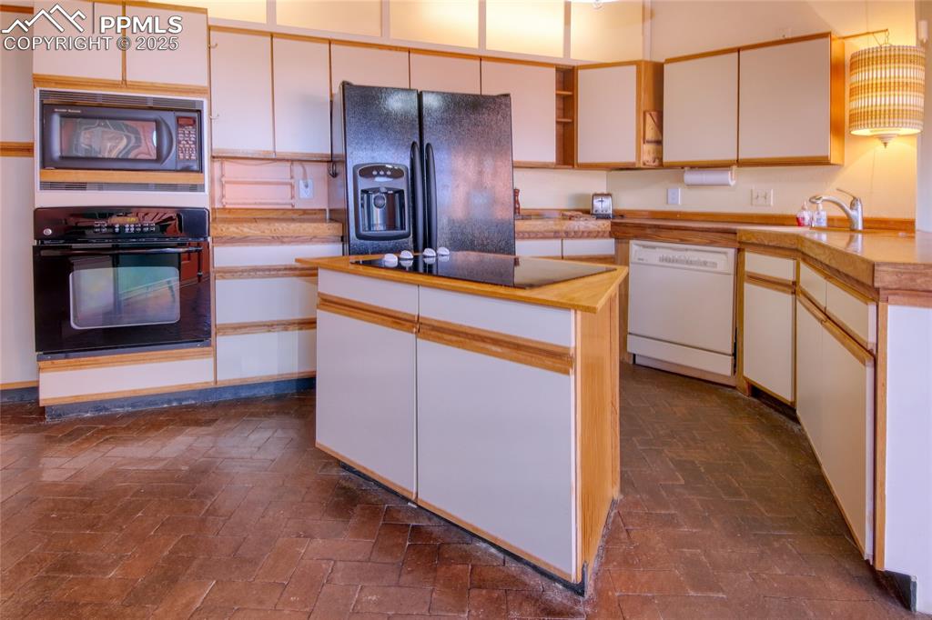 Image 8 of 33: Kitchen featuring a sink, brick floor, a kitchen island, black appliances, 