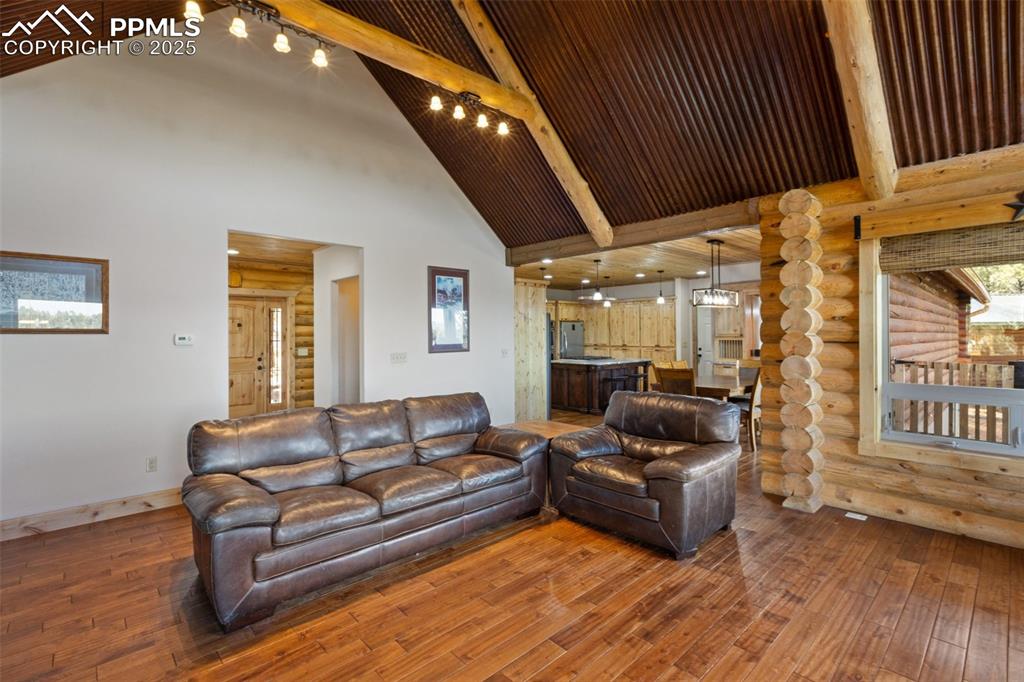 Image 14 of 46: Living area featuring log walls, beamed ceiling, wood-type flooring, and hi