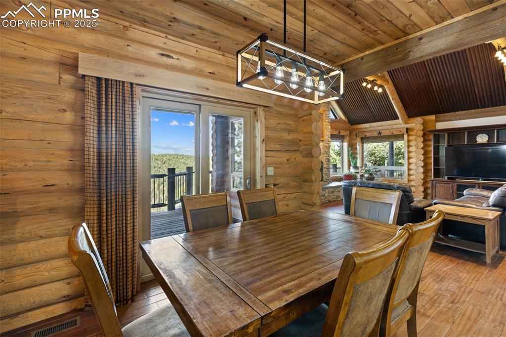 Image 19 of 46: Dining space with rustic walls, a chandelier, a wooden ceiling with exposed