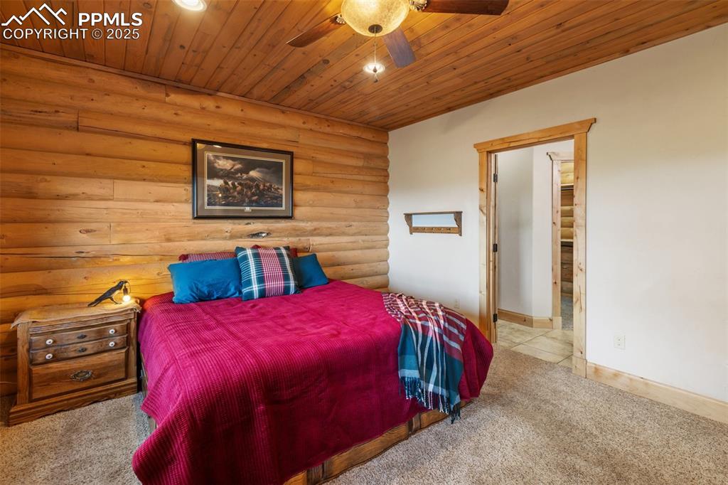 Image 23 of 46: Carpeted bedroom featuring log walls, wooden ceiling, ceiling fan, and rece
