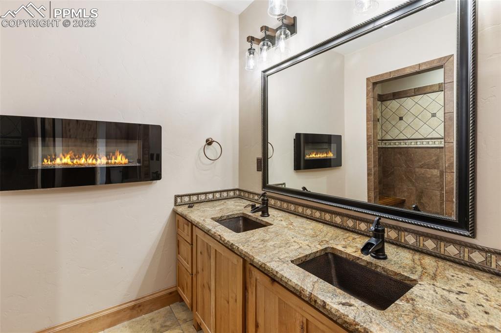 Image 25 of 46: Bathroom with a glass covered fireplace, double vanity, and a tile shower
