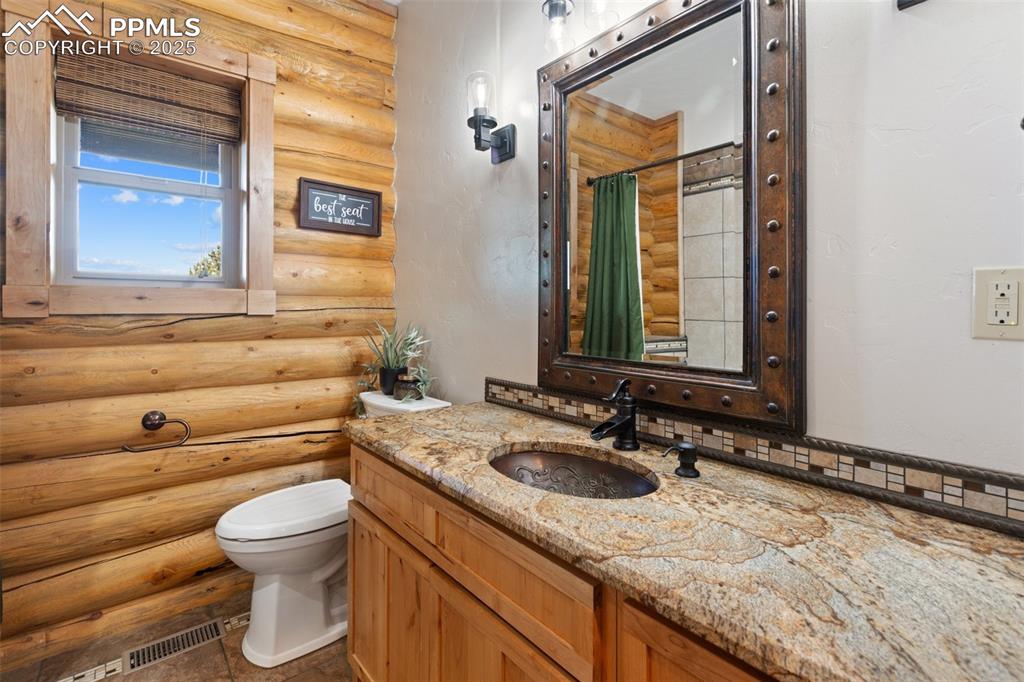 Image 28 of 46: Bathroom with log walls, curtained shower, and vanity