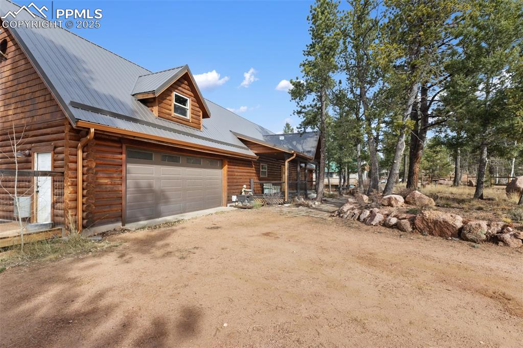 Image 7 of 46: View of front of home featuring dirt driveway, log siding, a metal roof, an