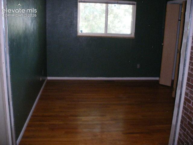 Image 19 of 35: Wood-finish flooring with white trim, dark green wall finish, and a window 
